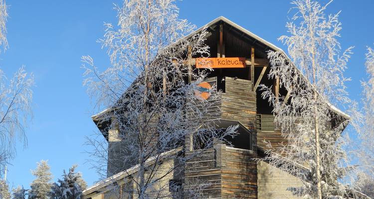 Bâtiment en bois rustique aux pointes givrées entouré de bouleaux glacés sous un ciel bleu.