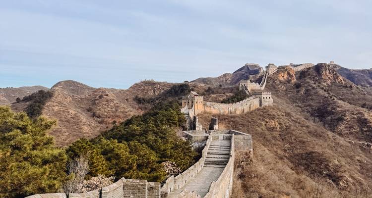 The Great Wall of China snakes over rugged brown hills under a pale sky.