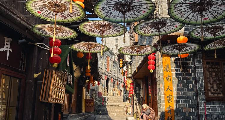Narrow stone alley decorated with hanging paper umbrellas and red lanterns in a traditional Chinese town.