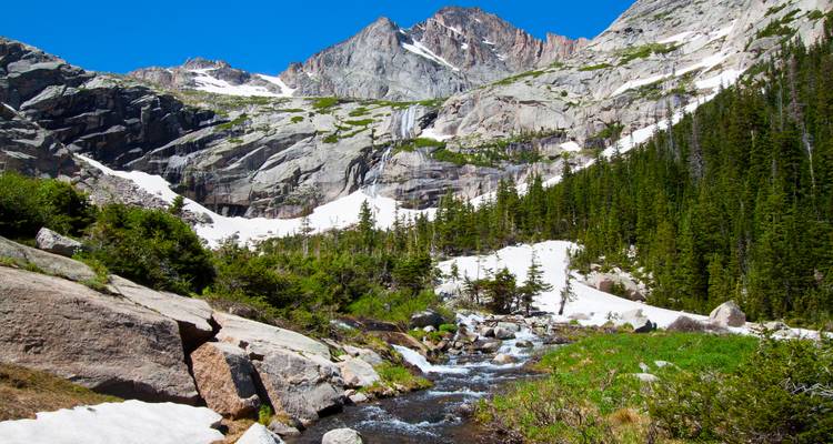 Ruisseau alpin coulant à travers une vallée enneigée sous des pics de granit escarpés et une forêt de conifères