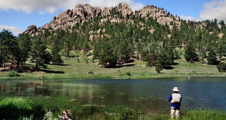 Deux pêcheurs debout près d'un lac forestier tranquille sous des collines rocheuses par une journée claire