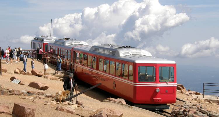 Des wagons de chemin de fer à crémaillère rouge vif perchés au sommet rocheux bien au-dessus des nuages.