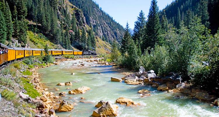Une locomotive à vapeur historique tirant des voitures jaunes le long d'une rivière à travers une forêt luxuriante de canyon du Colorado.
