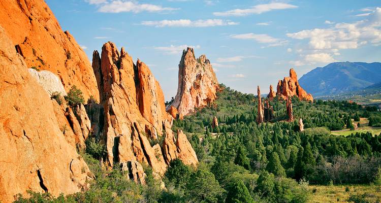 Les imposantes aiguilles de grès rouge du Garden of the Gods s'élevant au-dessus des pins verts sous un ciel bleu.