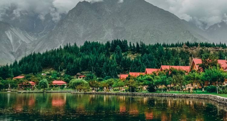 Crystal-clear lake reflecting red-roofed cottages, dense pine forest and high peaks