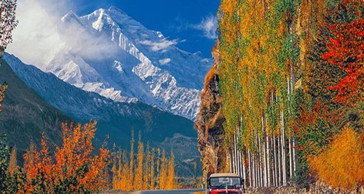 Vintage jeep driving along an autumn-colored valley beneath towering snowy peaks