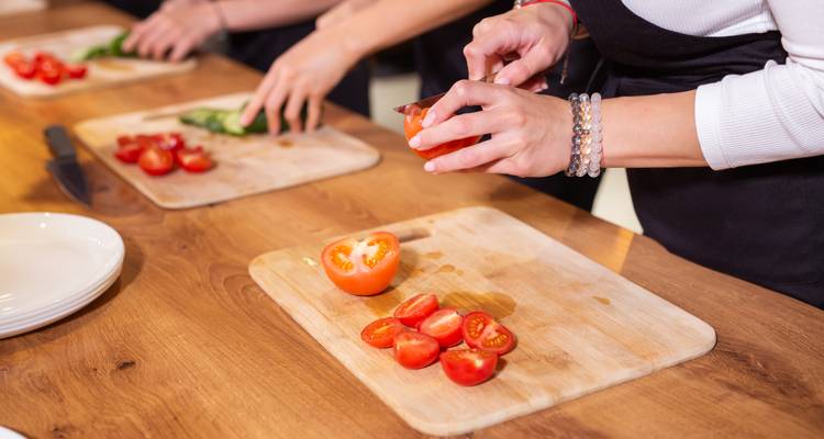 Gros plan sur des mains tranchant des tomates fraîches lors d'un cours de cuisine sur des planches à découper en bois.