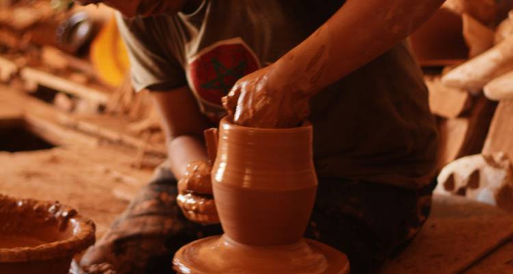 Un potier façonne de l'argile humide sur un tour qui tourne dans un atelier faiblement éclairé.
