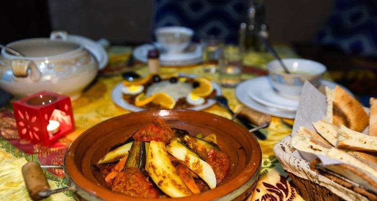 Gros plan d'un plat de tajine marocain traditionnel avec des légumes, du pain et un couvert de table.