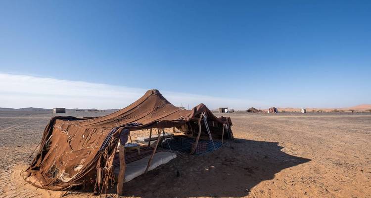 Tente nomade simple dressée sur une vaste plaine désertique aride sous un ciel bleu dégagé.