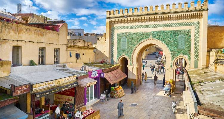 La porte Bab Bou Jeloud avec ses tours aux carreaux verts complexes surplombe une rue piétonne animée.