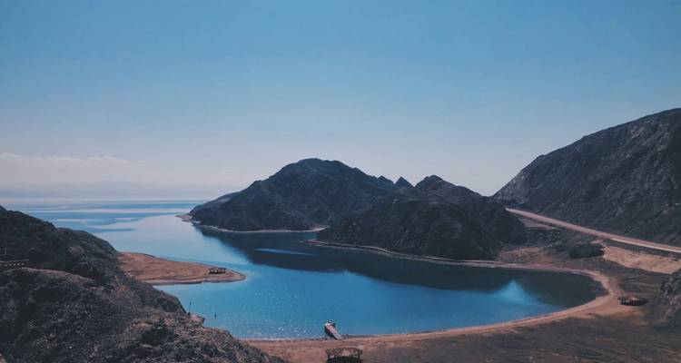 Lagon bleu cristallin entouré de montagnes rocheuses désertiques s'ouvrant sur la mer sous un ciel clair.
