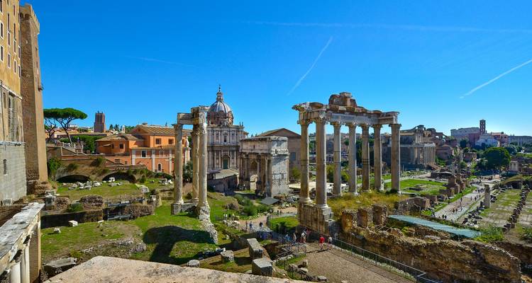 Vue panoramique sur le Forum romain avec des colonnes classiques et des basiliques sous un ciel bleu clair.