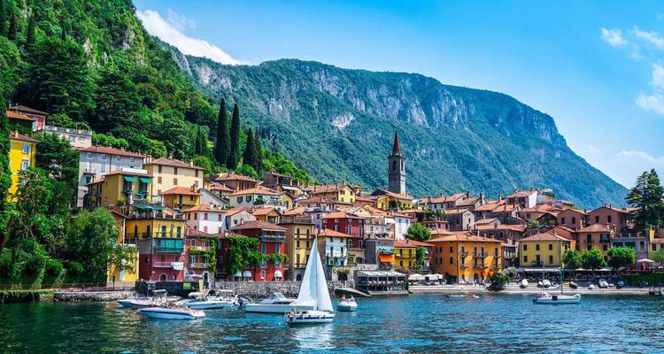 Des maisons aux couleurs vives et des voiliers bordent le front de mer d'un charmant village adossé à de hautes montagnes verdoyantes.