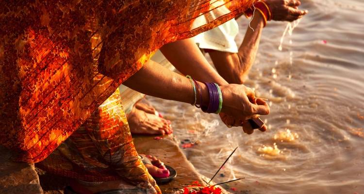 Handen van gelovigen in kleurrijke sari's die rivierwater scheppen tijdens een ritueel op stenen trappen