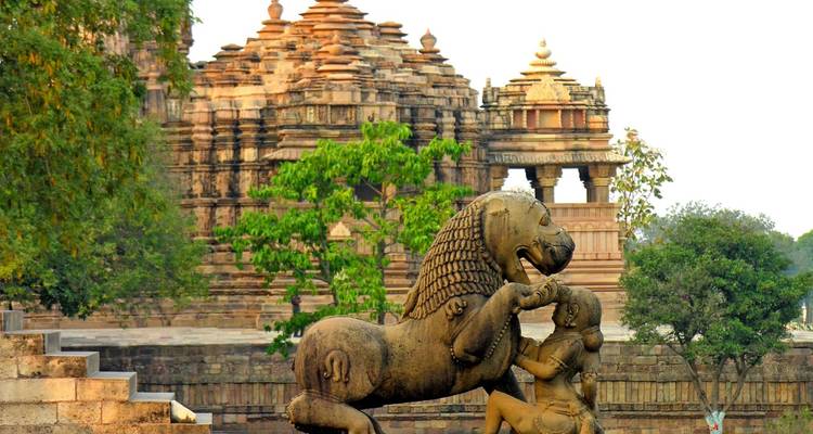Stenen sculptuur van een steigende leeuw met tempeltorens van Khajuraho wazig op de achtergrond