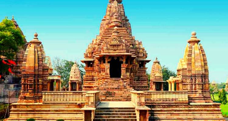 Vooraanzicht van een ingewikkeld gebeeldhouwde zandstenen tempel van Khajuraho tegen een heldere blauwe hemel