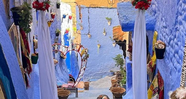 Smalle blauwe steeg in Chefchaouen versierd met rode bloemen en hangende potten