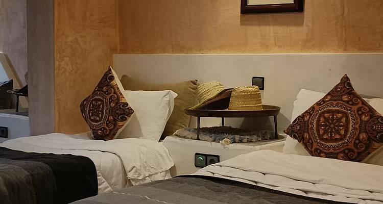 Gezellige tweepersoonsbedden met gedessineerde kussens en strooien hoeden in een gastenverblijf in Marokkaanse stijl