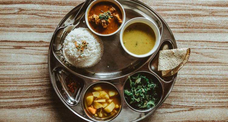 Traditionelles nepalesisches Thali-Gericht angerichtet auf einem Metallteller mit Reis, Currys und Gemüse.
