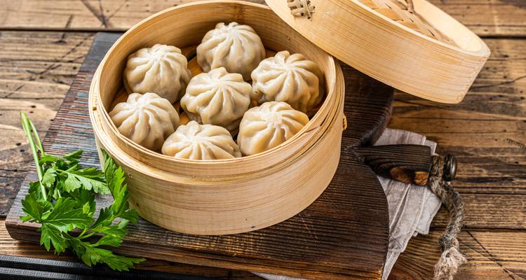 Gedämpfte nepalesische Momos ordentlich in einem Bambuskorb auf rustikalen Holzbrettern angerichtet.
