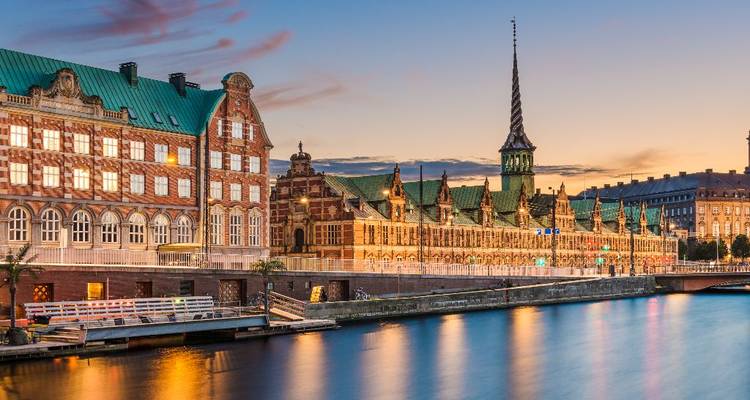 Lueur crépusculaire sur le Børsen historique de Copenhague et canal reflétant des cieux colorés.