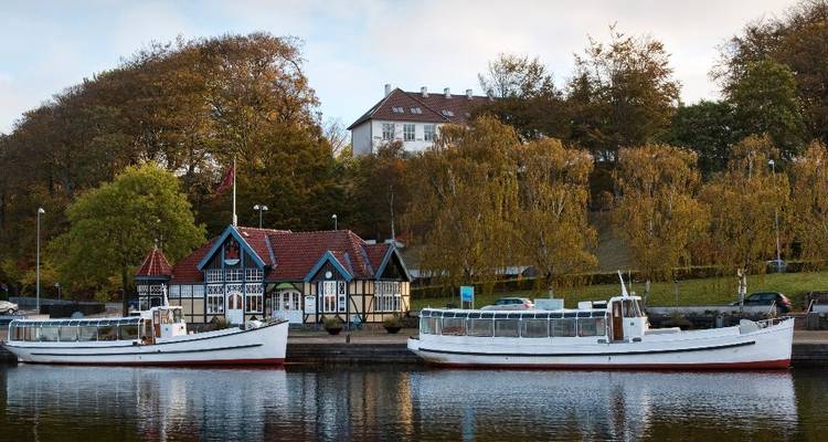 Deux bateaux d'excursion blancs amarrés à côté d'un cottage pittoresque en bois et d'arbres d'automne.