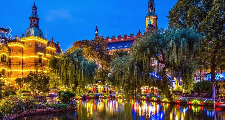 Vue nocturne des jardins de Tivoli avec des lumières colorées se reflétant dans un étang tranquille.
