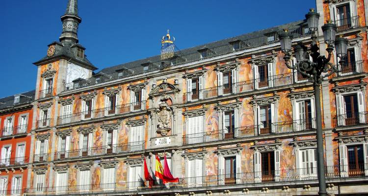Colorful frescoed facade with balconies and coats of arms on Plaza Mayor building against clear blue sky.