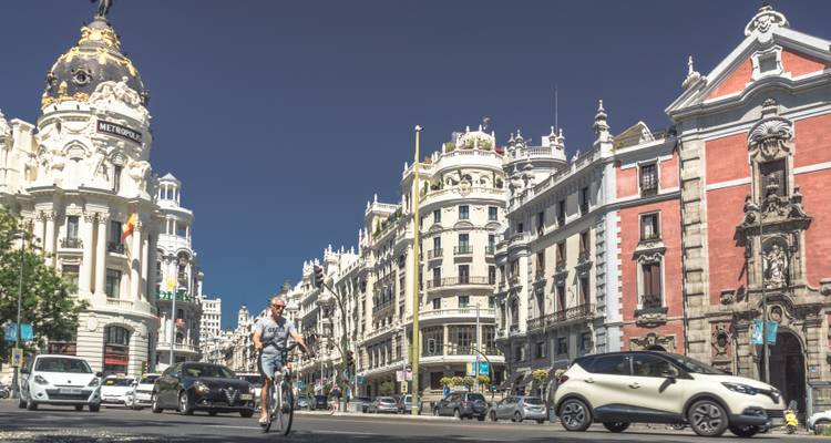 Busy Gran Vía avenue lined with ornate buildings, cars and cyclist on sunny day in Madrid.