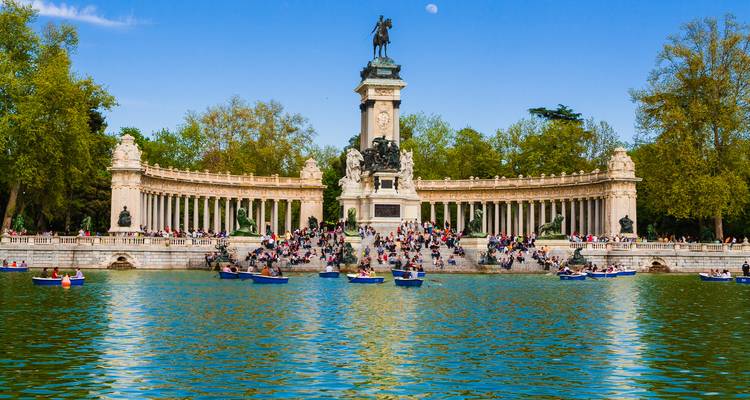 Crowds enjoying rowboats on lake before grand semicircular monument in El Retiro Park, Madrid.