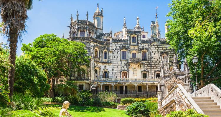 Palacio neomanuelino ornamentado de la Quinta da Regaleira rodeado de exuberantes jardines bajo un cielo azul brillante
