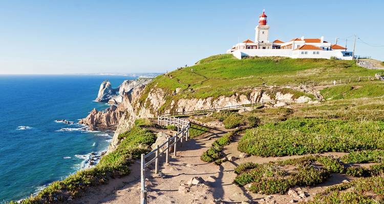 Acantilado costero pintoresco con un faro de techo rojo que domina el océano Atlántico azul profundo.