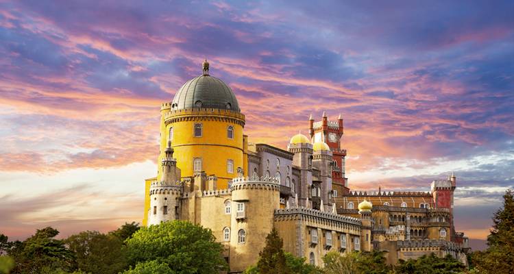 El colorido Palacio da Pena se alza sobre árboles verdes bajo un cielo dramático de atardecer.