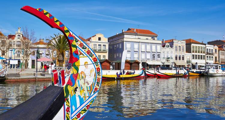 Proa pintada de un barco moliceiro con edificios históricos ribereños bajo cielo azul.