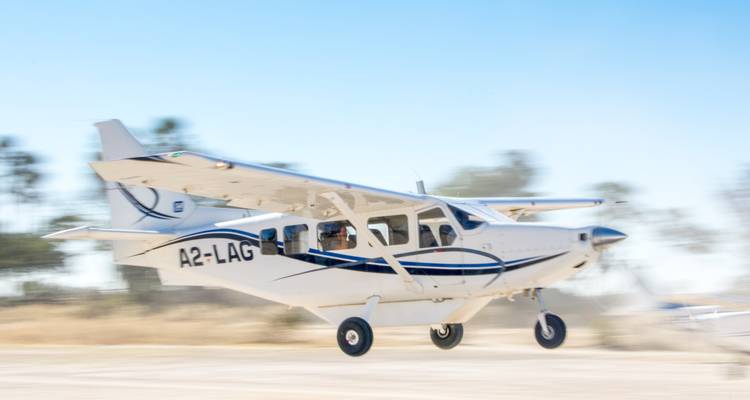 Light aircraft speeding up on sandy runway in bright sunlight.
