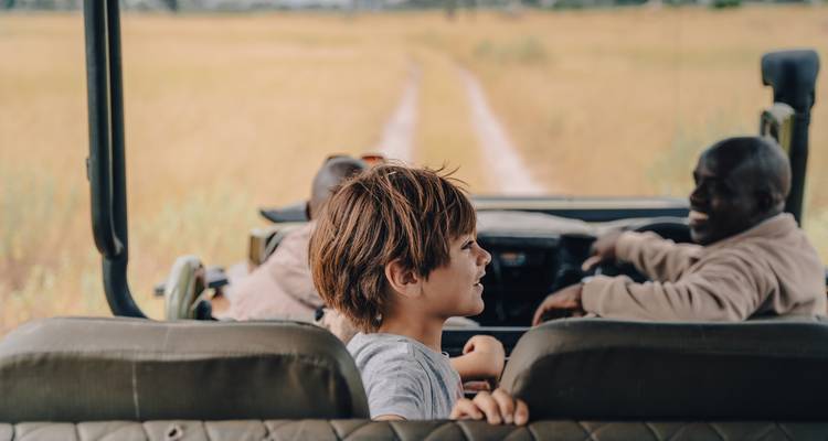 Side view of child and guide chatting while driving in open safari jeep along dirt track.