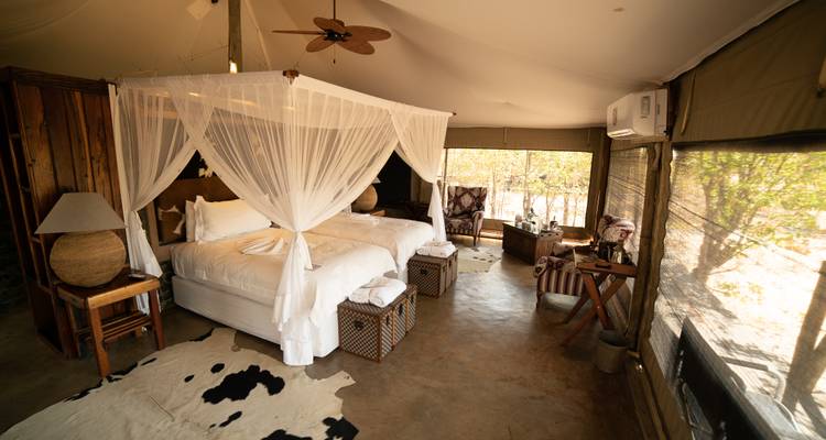 Tienda de safari de lujo con cama con dosel, muebles rústicos y alfombras de piel de vaca.