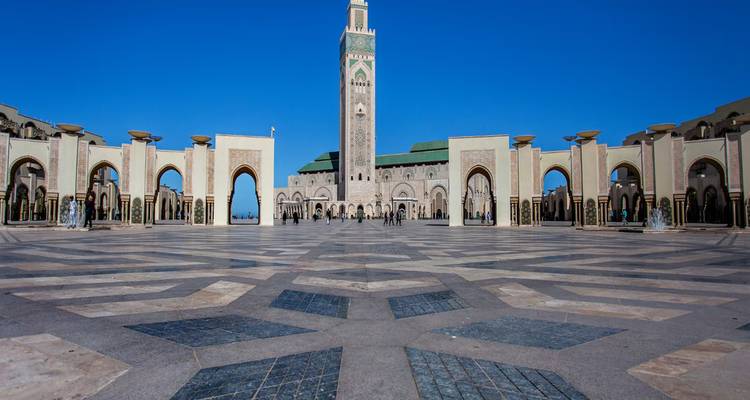 Uitgestrekt marmeren binnenplein dat leidt naar de torenhoge Hassan II-moskee onder een diepblauwe hemel.