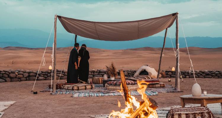 Woestijnkamp met een knetterend vuur en lage Berbertenten onder de schemerende hemel.