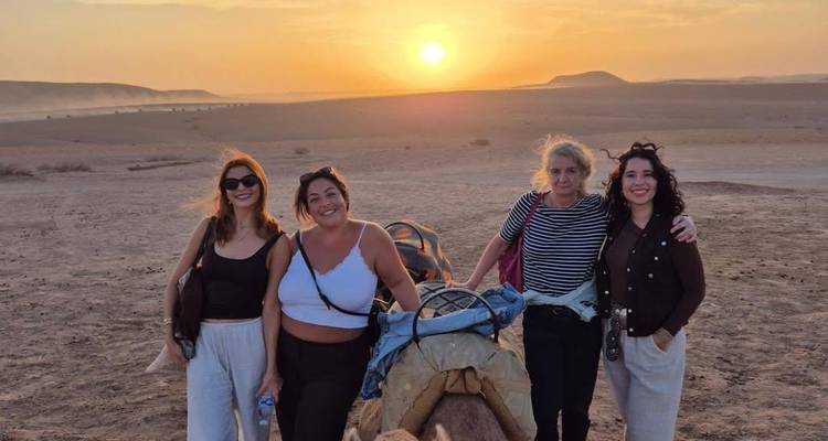Groep vrouwen glimlacht voor brede woestijnvlaktes tijdens gouden zonsondergang.