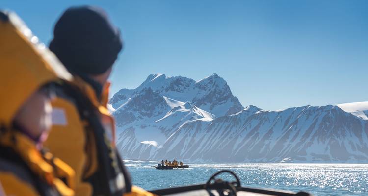 Un pasajero en una zodiac mira hacia las montañas cubiertas de nieve mientras otro bote se acelera a través del agua brillante.