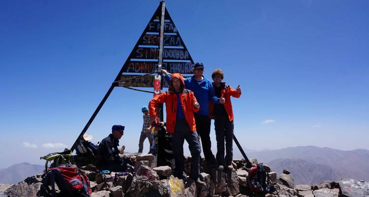 Klimmers die vieren naast de metalen toppiramide op de piek van Mount Toubkal.
