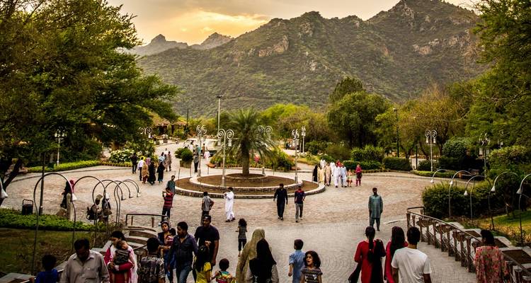 Familles et visiteurs se promenant dans un parc paysager avec les collines de Margalla en toile de fond au crépuscule