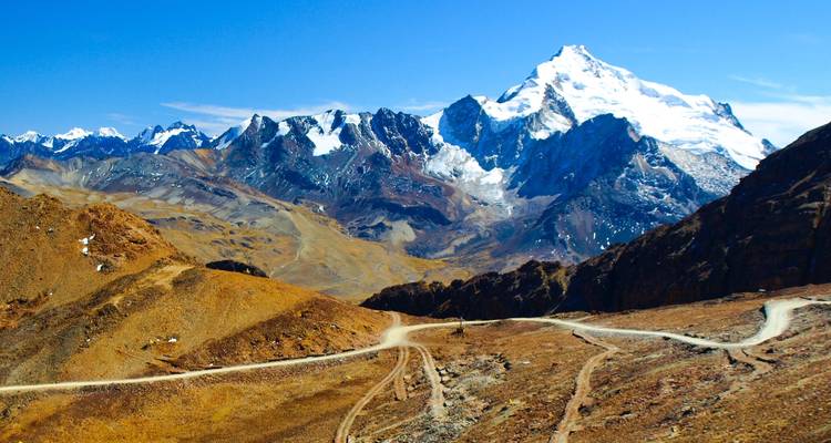 Andes bergketen met sneeuwbedekte piek die uittorent boven kronkelende onverharde wegen en dorre hellingen.