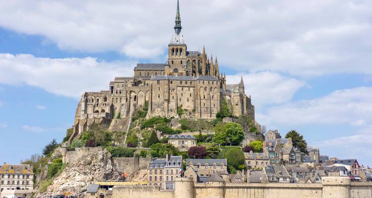 L'abbaye emblématique du Mont Saint-Michel s'élevant au-dessus des vasières avec son reflet dans l'eau.