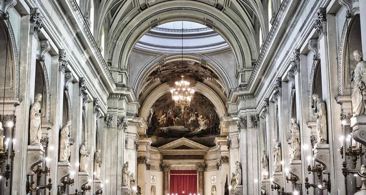 Grand baroque-style cathedral interior featuring high vaulted arches, marble columns, chandeliers and detailed frescoes.