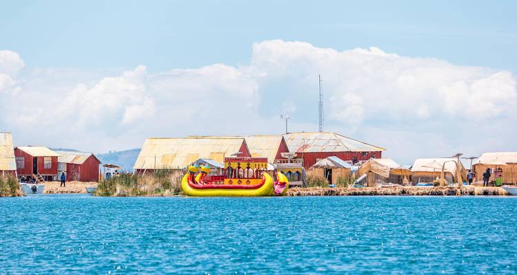Un bateau de roseau jaune vif et rouge flotte près des îles rustiques d'Uros sur les eaux bleues scintillantes du lac Titicaca.