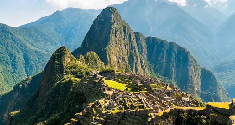Vue panoramique emblématique des ruines du Machu Picchu avec le Huayna Picchu qui s'élève majestueusement derrière sous un ciel dégagé.