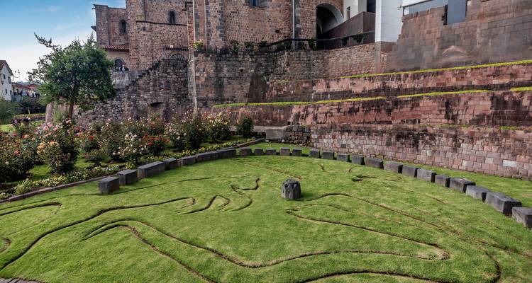 Pelouse entretenue et motif de serpent en pierre devant les murs inca-espagnols du Qorikancha à Cusco.